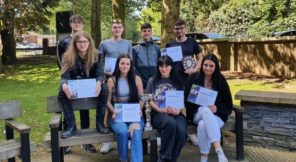 Seated and standing public services students holding certificates outside the Bangor campus.